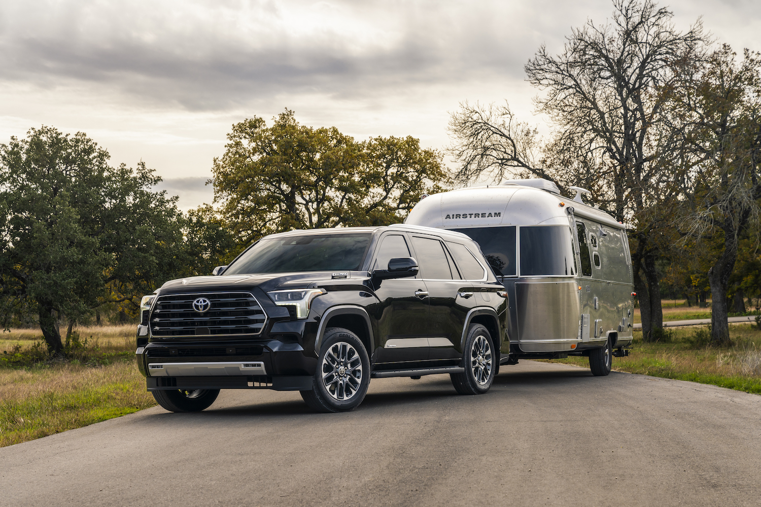 Black Toyota Sequoia Limited hybrid SUV parked on a dirt road with an Airstream trailer, trees visible in the background.