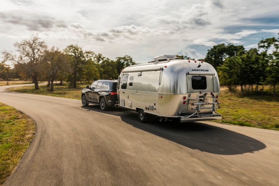 A 2023 Toyota Sequoia full-size SUV pulling an airstream camper trailer down a rural road.