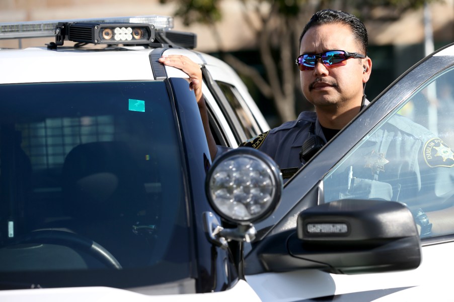 A police officer stands next to his SUV interceptor with its rooftop ALPR scanning camera.