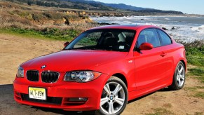 A red BMW 128i sits on a coastline road.