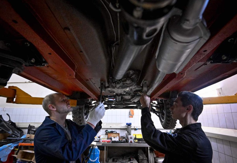 Two people inspecting a car that could be leaking water. 