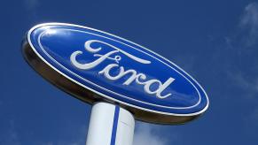 The blue Ford logo as it appears on a large sign above a dealership, the sky visible in the background.