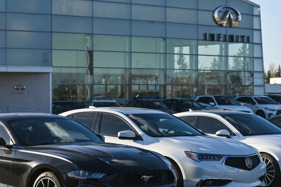 An Infiniti dealership parking lot with many cars lined up. Can I ask a dealer to remove its branding stickers from my car?