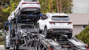 Several cars loaded on a transport trailer, trees and buildings visible in the background.