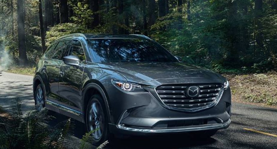 A gray 2023 Mazda CX-9 midsize SUV is driving on the road. 