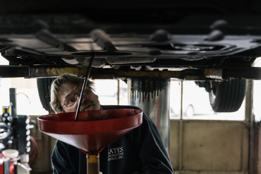 A mechanic is watching the oil spill from an oil pan