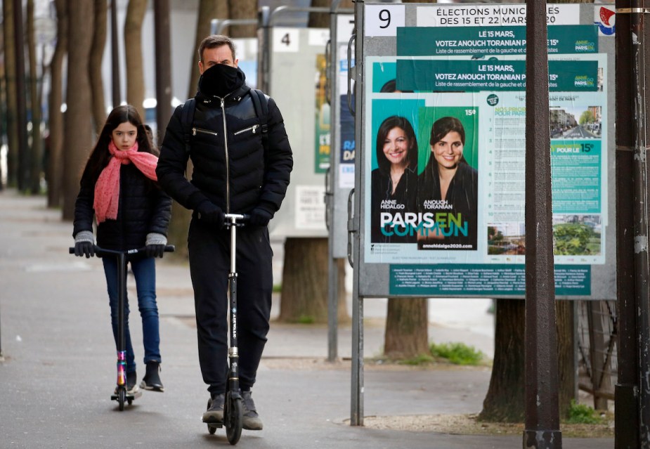 People riding on scooters, potentially a Varla Pegasus, down a city sidewalk. 