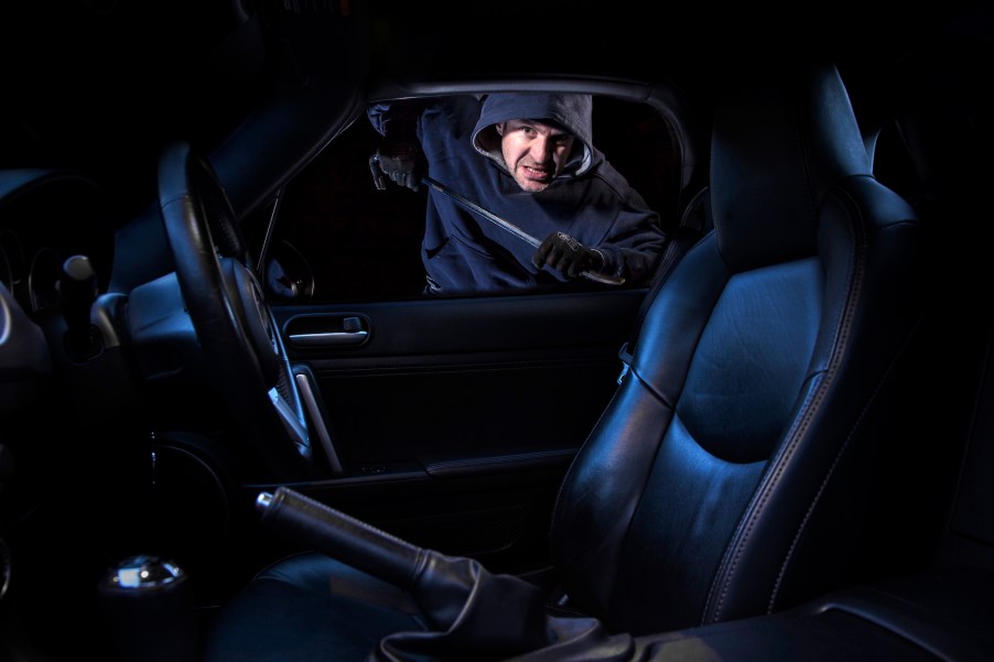 A man breaking into a parked car at night.