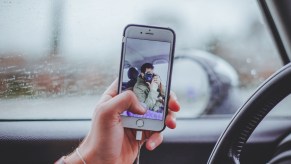 Person taking a selfie photo with a cell phone while driving a car, highlighting whether or not it's illegal