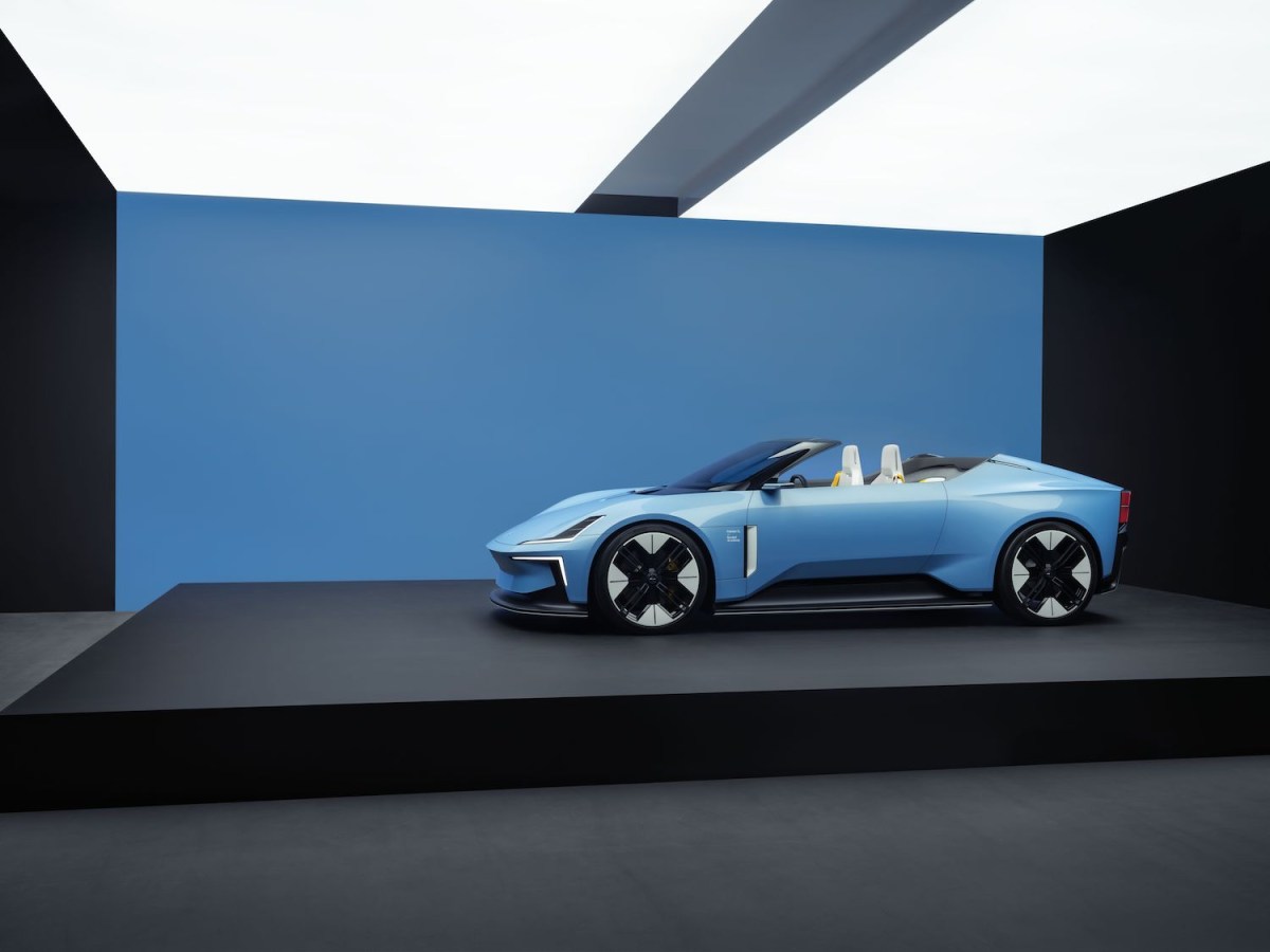 A light blue Polestar 6 roadster parked against a dark blue wall