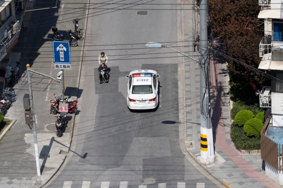 A street scene in China includes a man on a bike and a police sedan with numbers on its roof.