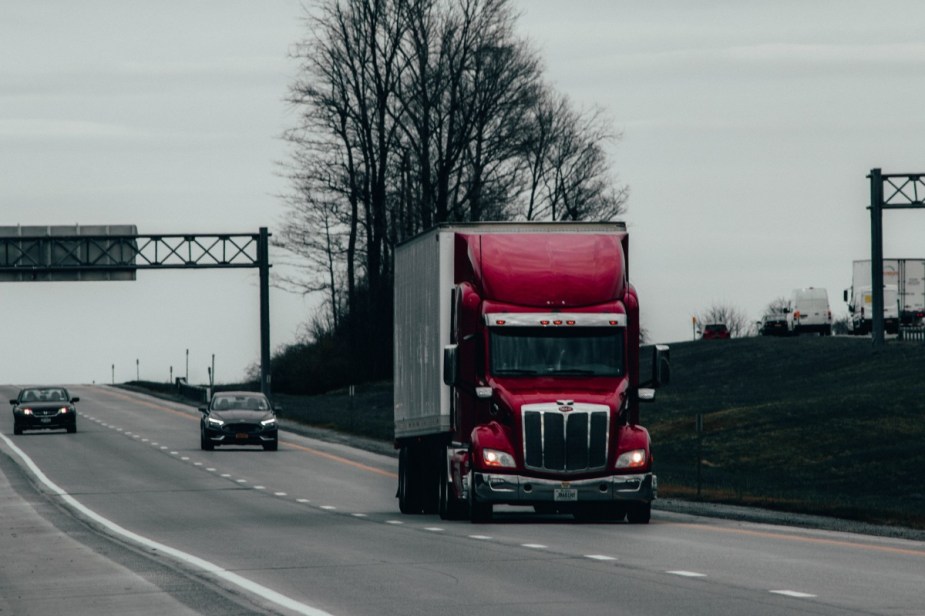 Red semi-truck driving on highway, highlighting why trucks have to stop at weigh stations