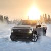 A 2022 Ford F-150 Lightning electric truck driving on snow with its headlights on as the sun sets in Alaska