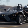 A black Polaris Slingshot drives down a highway.