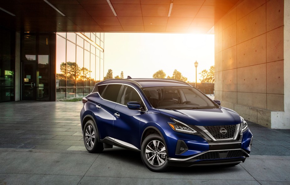 A blue 2023 Nissan Murano midsize crossover SUV parked outside a glass panel office building as the sun sets