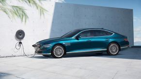 A teal Genesis Electrified G80 midsize EV sedan model plugged into a charging station