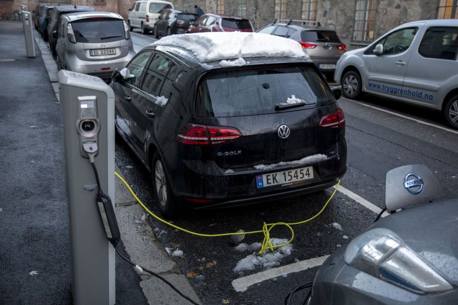 Electric cars, including a VW e-Golf, covered in snow, plugged into public charging stations in Oslo, Norway