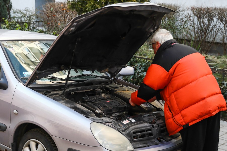 A person looking under the hood, potentially going to administer an engine cleaner.