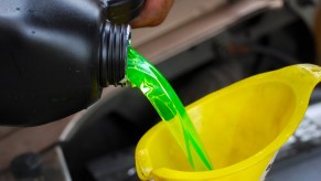 A jug of coolant is being poured into a yellow funnel under an open car hood.