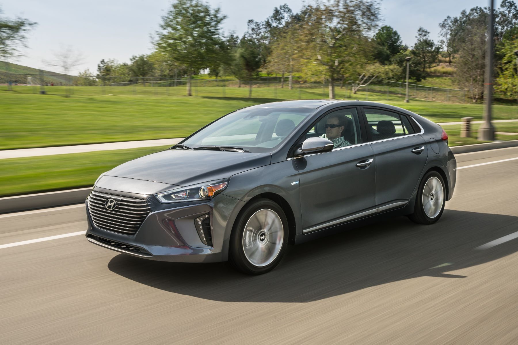 A gray 2018 Hyundai Ioniq Hybrid compact sedan driving past a park