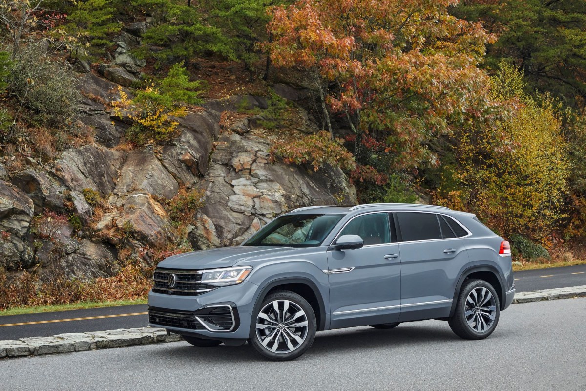 A gray 2022 Volkswagen Atlas Cross Sport midsize SUV parked near a highway cliffside of rocks, moss, and trees. This model is one of the best midsize SUVs in 2023 to buy.