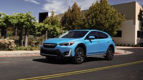 A light blue 2023 Subaru Crosstrek Hybrid compact SUV model driving past a nature enclosure