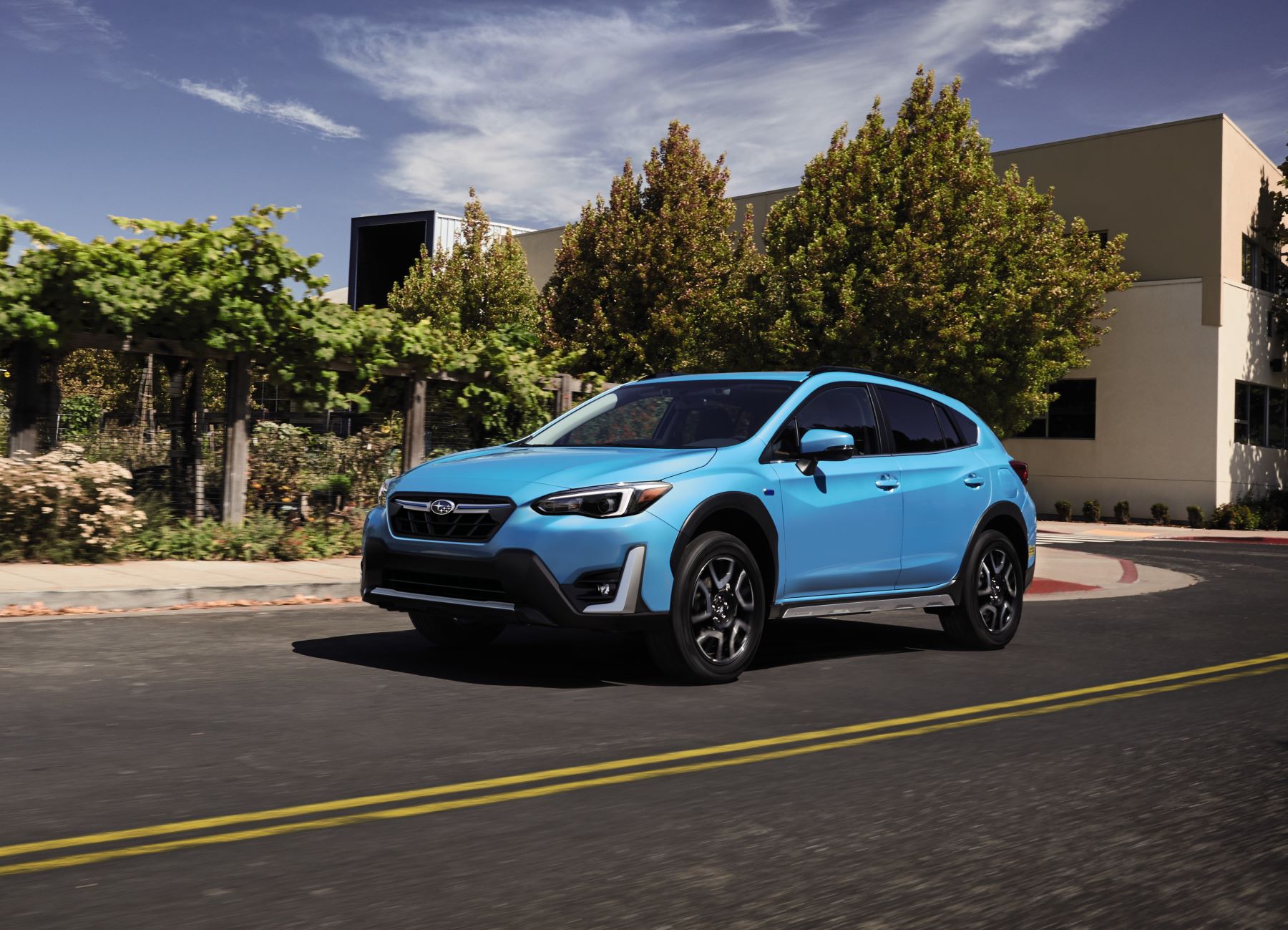 A light blue 2023 Subaru Crosstrek Hybrid compact SUV model driving past a nature enclosure