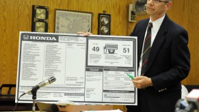 A Dealership sticker that displays the information regarding the car, including the fuel economy ratings, being held by a man in a wood paneled office.