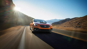 An orange 2022 Subaru WRX driving on a desert highway near rolling hills as the sun glares in a cloudless sky