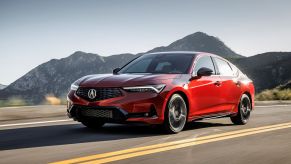 A red 2023 Acura Integra A-Spec compact liftback driving down a highway framed by a mountain range