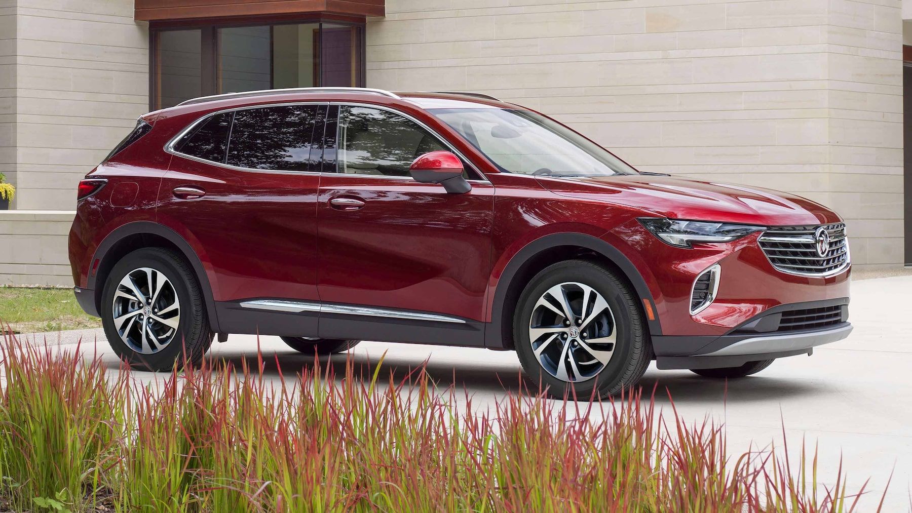 A red 2023 Buick Envision premium midsize SUV model parked on the driveway of a luxury home