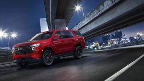 A red 2023 Chevy Tahoe RST Performance Edition full-size SUV driving under a highway overpass at night