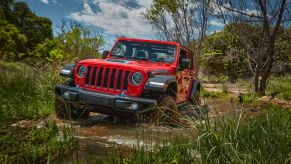 A red 2023 Jeep Wrangler 4xe plug-in hybrid (PHEV) model driving through a swamp