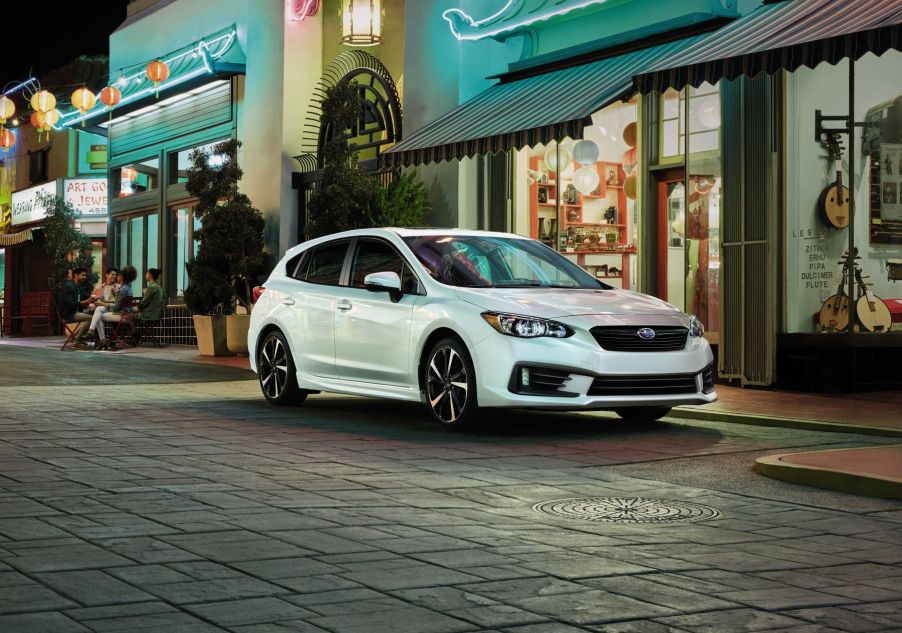 A white 2022 Subaru Impreza compact sedan parked on a downtown tiled street at night near open shops