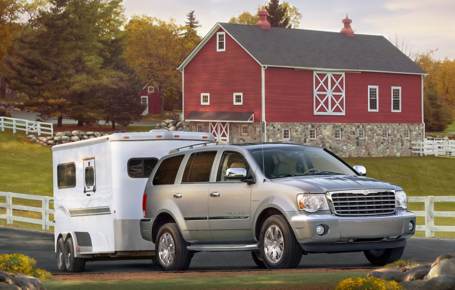 A 2009 Chrysler Aspen full-size hybrid, AWD, HEMI V8 powered luxury SUV pulling a horse trailer in front of a barn.