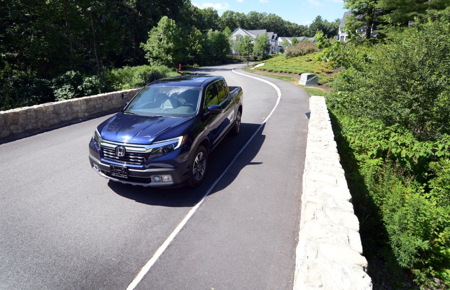 A reliable midsize Honda Ridgeline pickup truck driving across a bridge, a windy country road visible in the background.