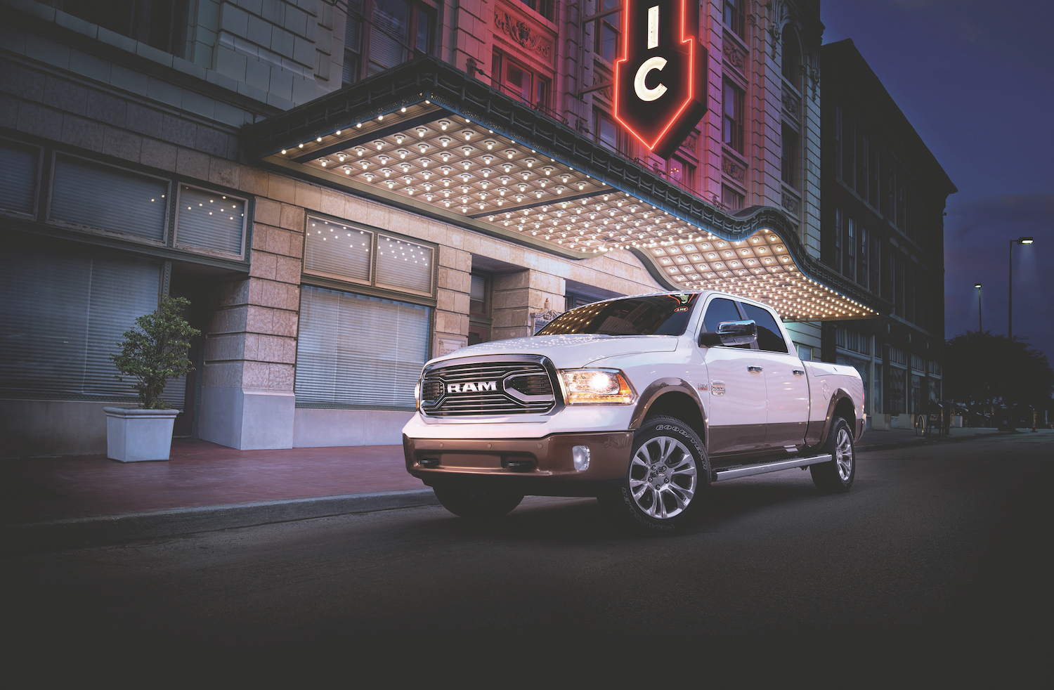 White Ram pickup truck parked in front of a city building with neon lights.