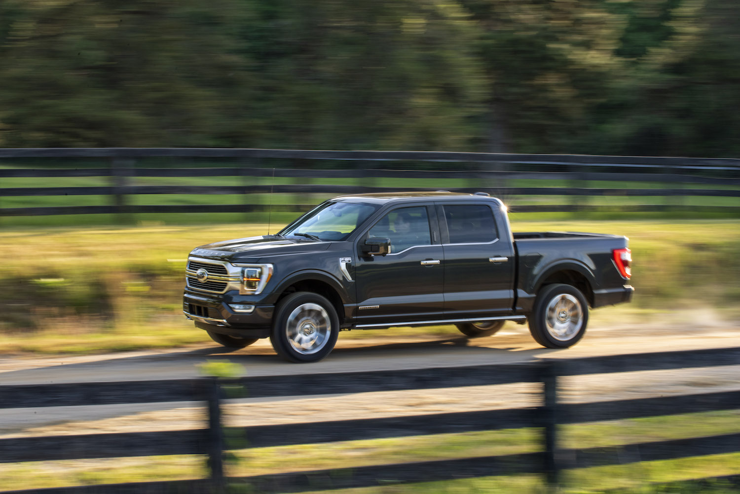 Black Ford F-150 hybrid PowerBoost pickup truck driving down a country lane, fences on both sides.