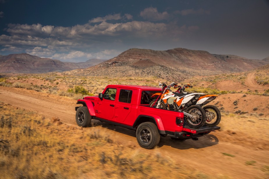 Jeep Gladiator pickup truck hauling dirt bikes, desert mountains visible in the background.