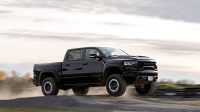 A black 2021 Ram 1500 TRX performance supercharged full-size pickup truck jumping off a dirt ramp