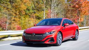 A red 2021 Volkswagen Arteon liftback luxury sedan model driving on a highway near autumn trees