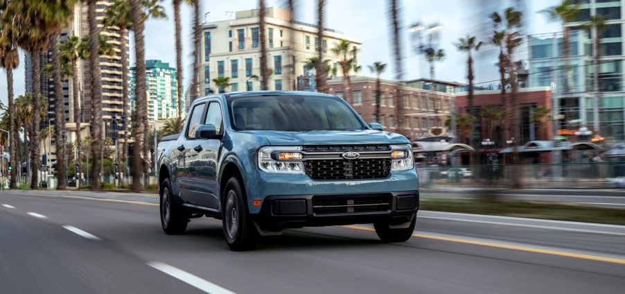 A blue-gray 2022 Ford Maverick Hybrid XLT compact pickup truck driving past palm trees