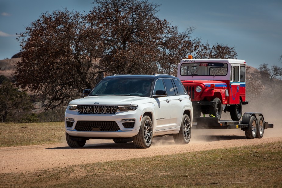 A costly Jeep Grand Cherokee towing a vintage Jeep on a flat trailer.