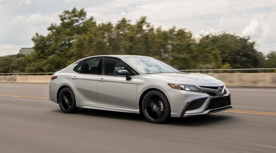 A white 2022 Toyota Camry Hybrid driving in an outdoor wooded environment. 