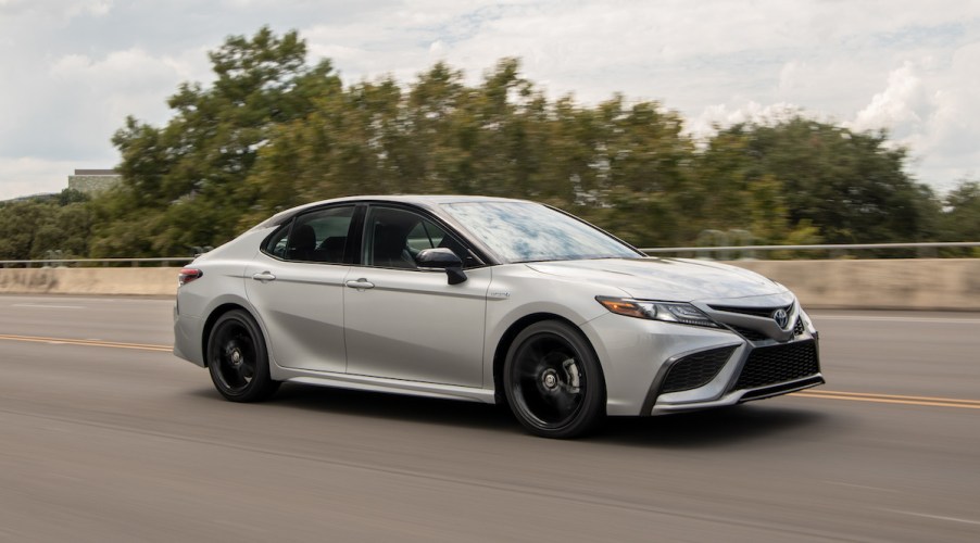 A white 2022 Toyota Camry Hybrid driving in an outdoor wooded environment.