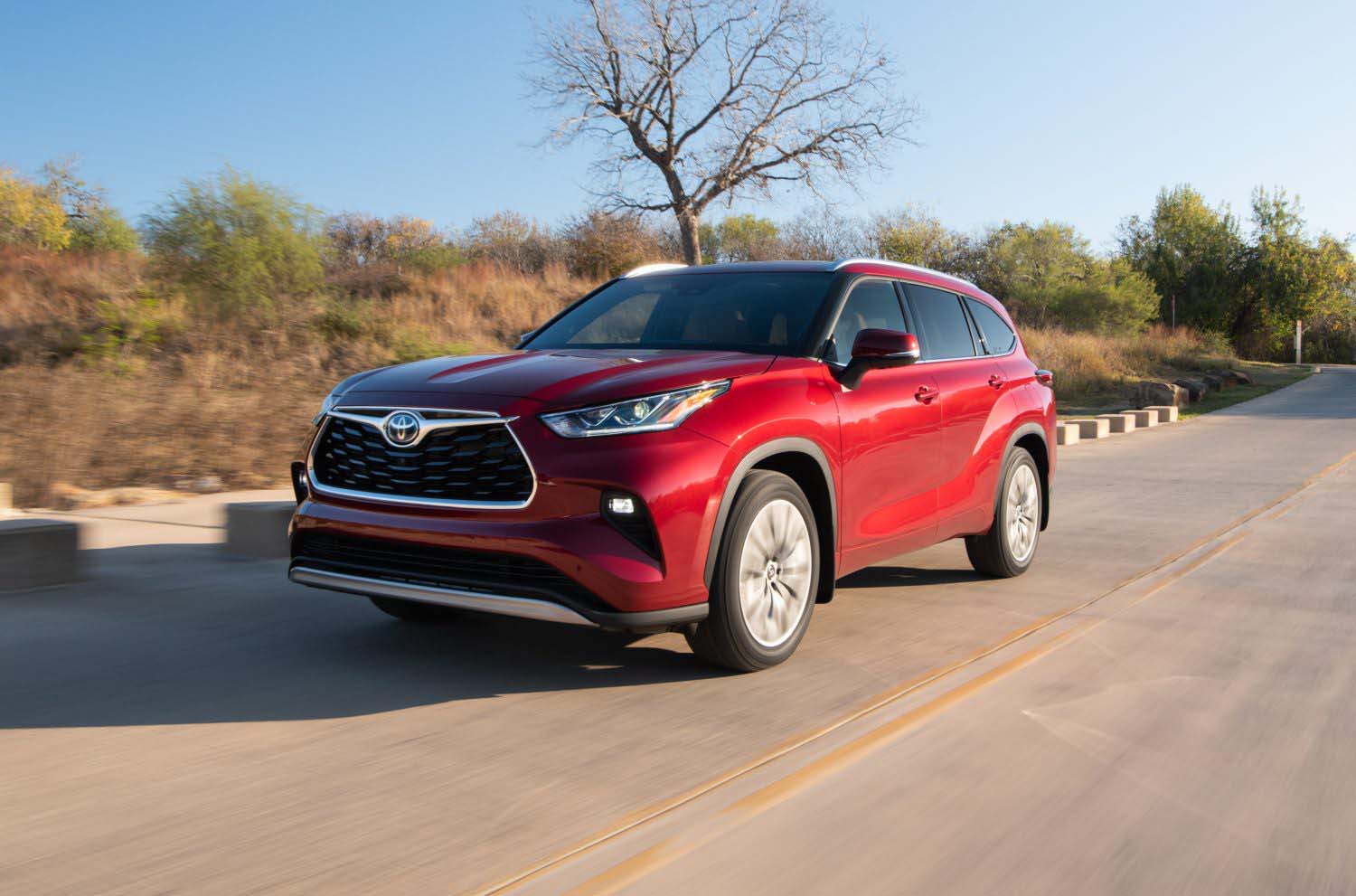 Red Toyota Highlander driving down the road trees visible in the background.