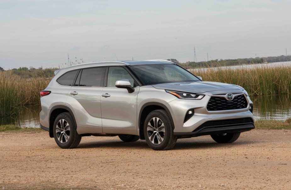 Silver Toyota Highlander hybrid crossover SUV vehicle parked in front of a lagoon, power-lines visible in the background.