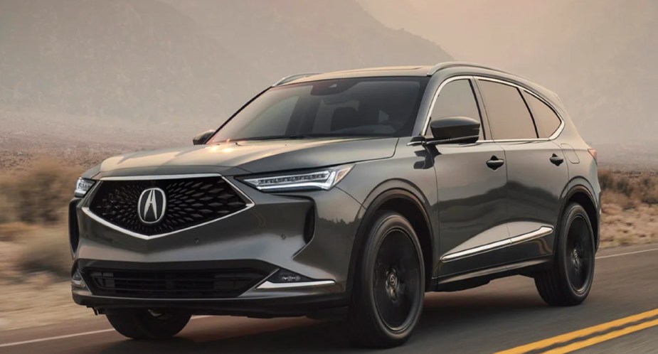 A gray 2023 Acura MDX luxury midsize SUV is driving on the road. 