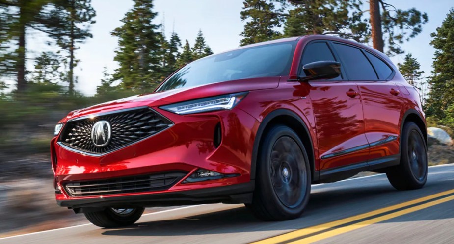 A red 2023 Acura MDX is driving on the road. 