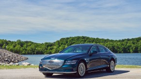 A blue 2023 Electrified Genesis GV80 parked in front of body of water.